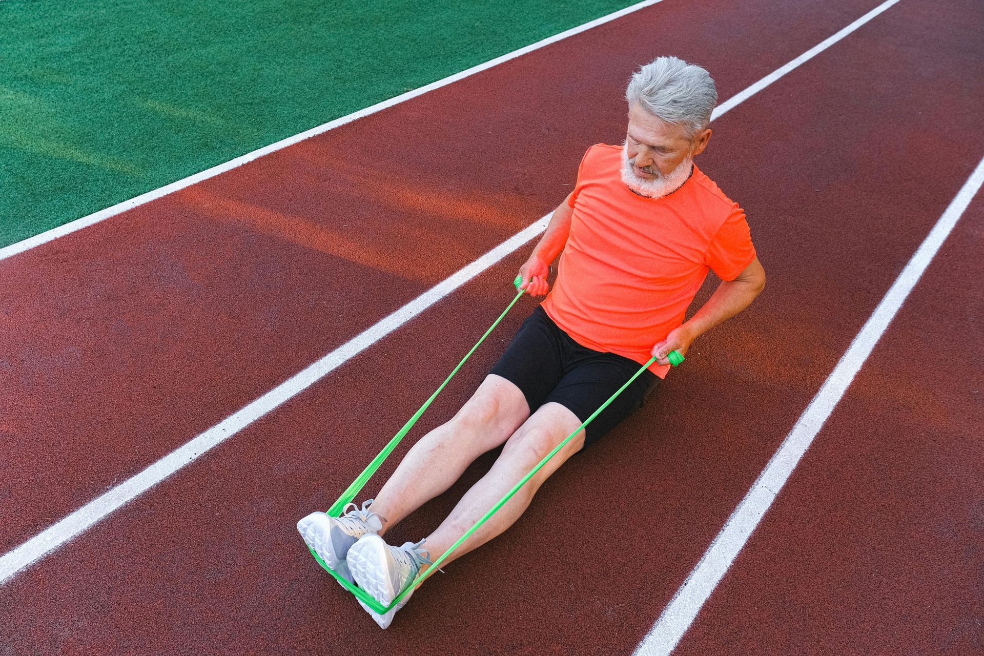 A man is sitting on a track using a resistance band