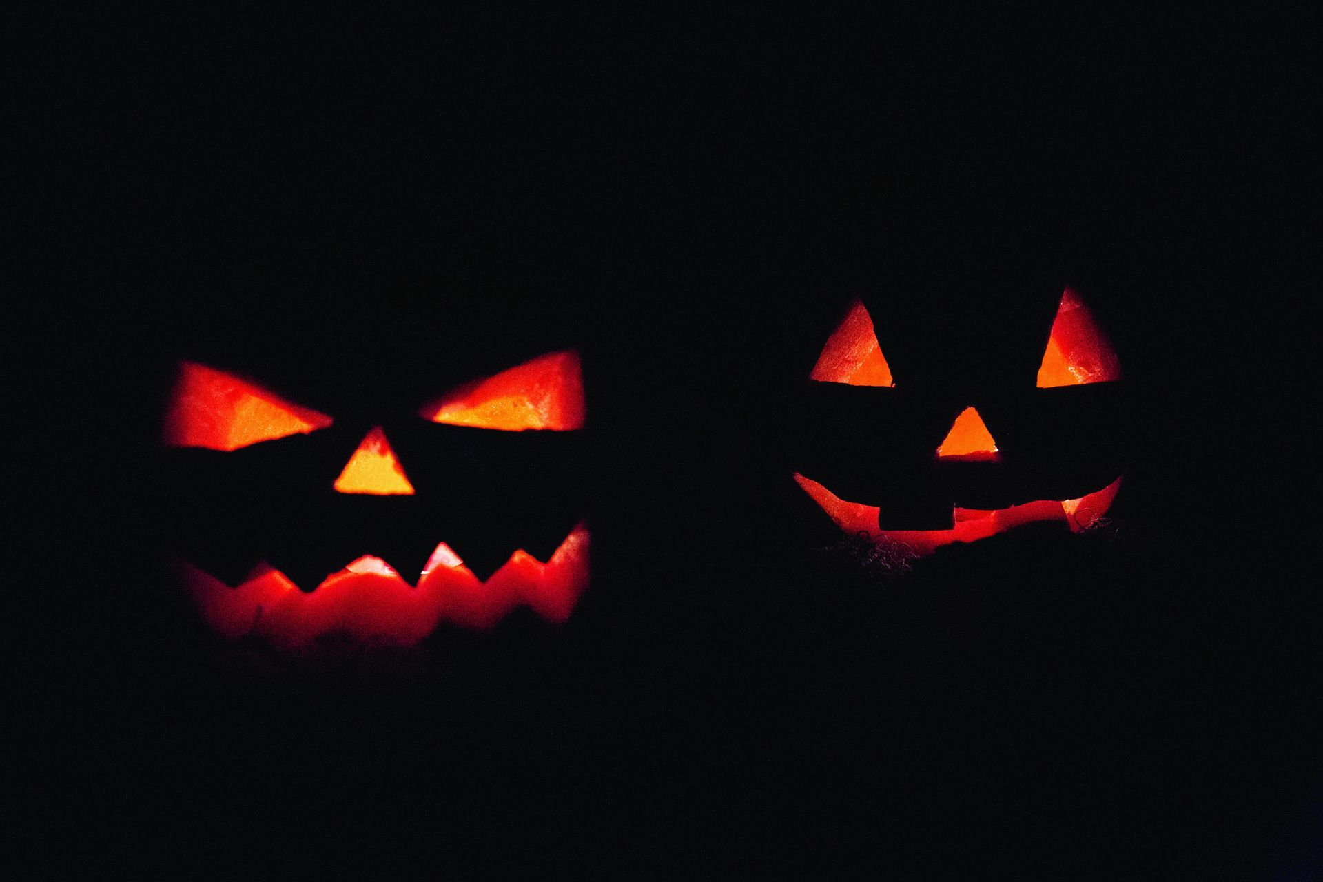 Two carved halloween pumpkins are lit up in the dark.