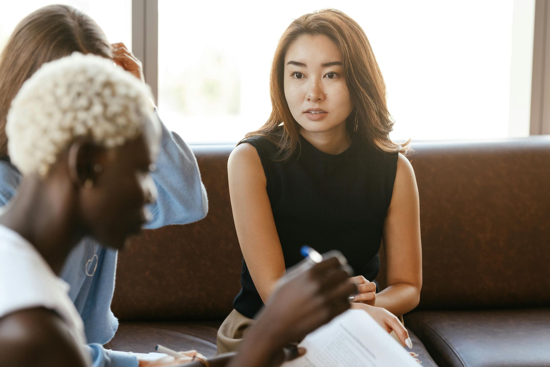 Woman in black top sitting with other people, focused expression.