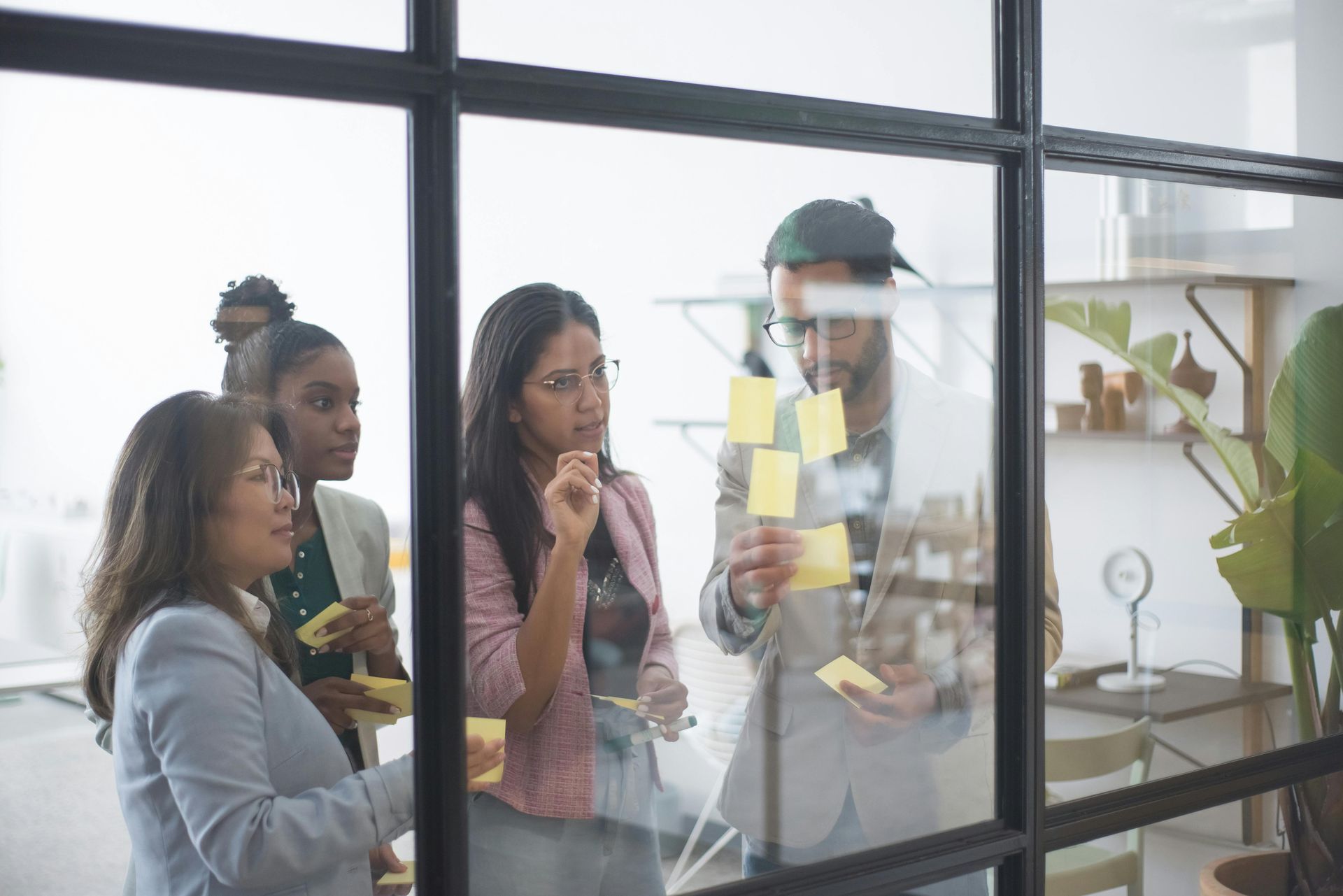 Group of people in an office looking at sticky notes on a glass wall, discussing ideas.