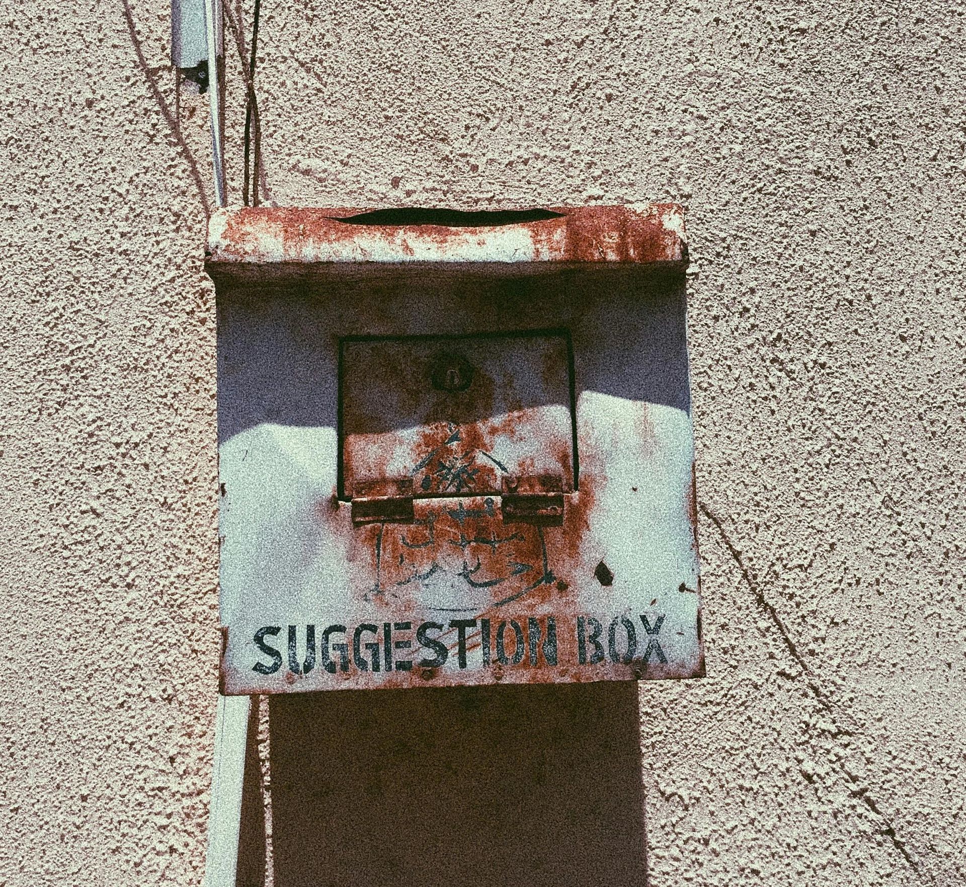 A rusty suggestion box is attached to a wall