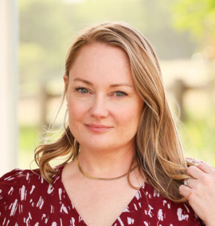 A woman in a red shirt is smiling and holding her hair.