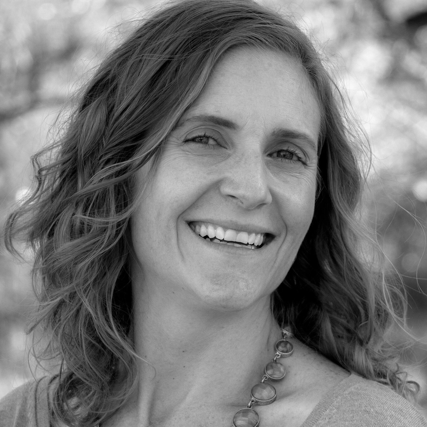 A woman with long hair is smiling in a black and white photo.