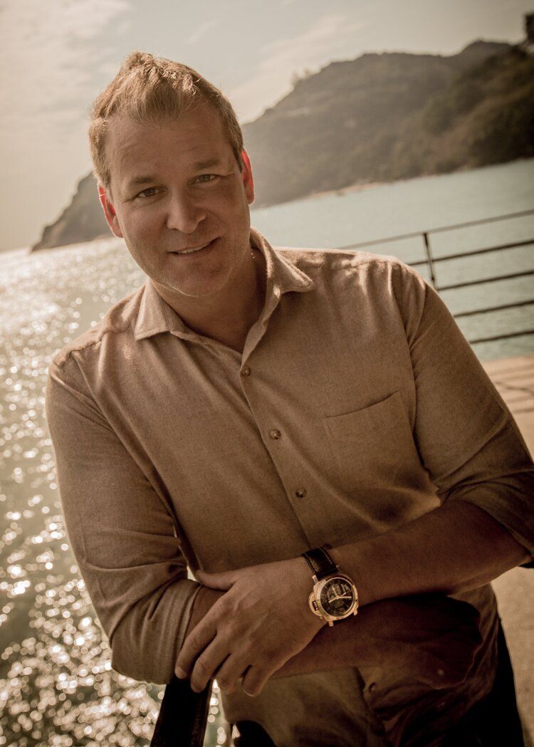 Headshot of Shawn Thomas, leaning against a railing, arms crossed, with water in the background.