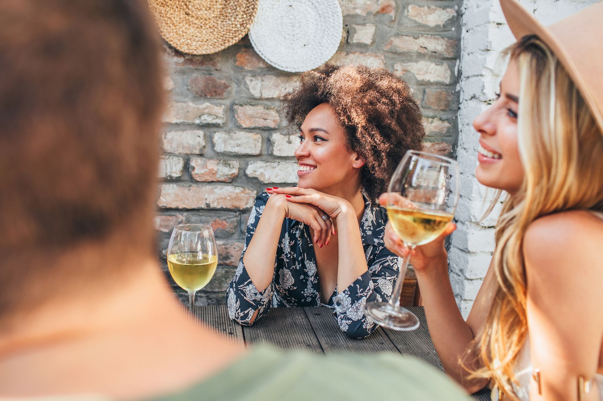 Three people enjoying wine outdoors; two women smile, one with curly hair.
