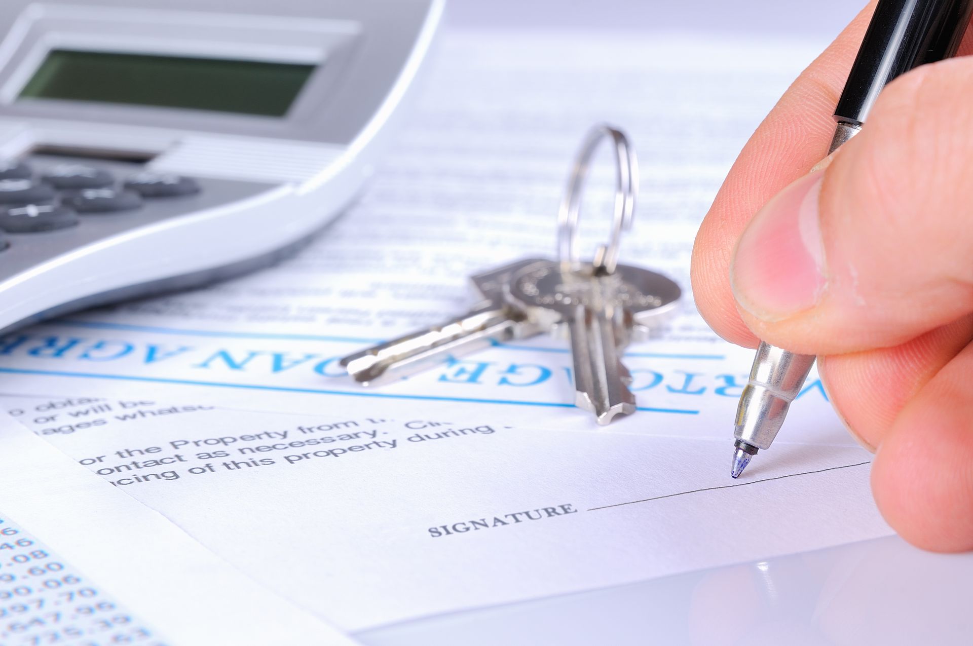 A person is signing a lease agreement next to a calculator and keys