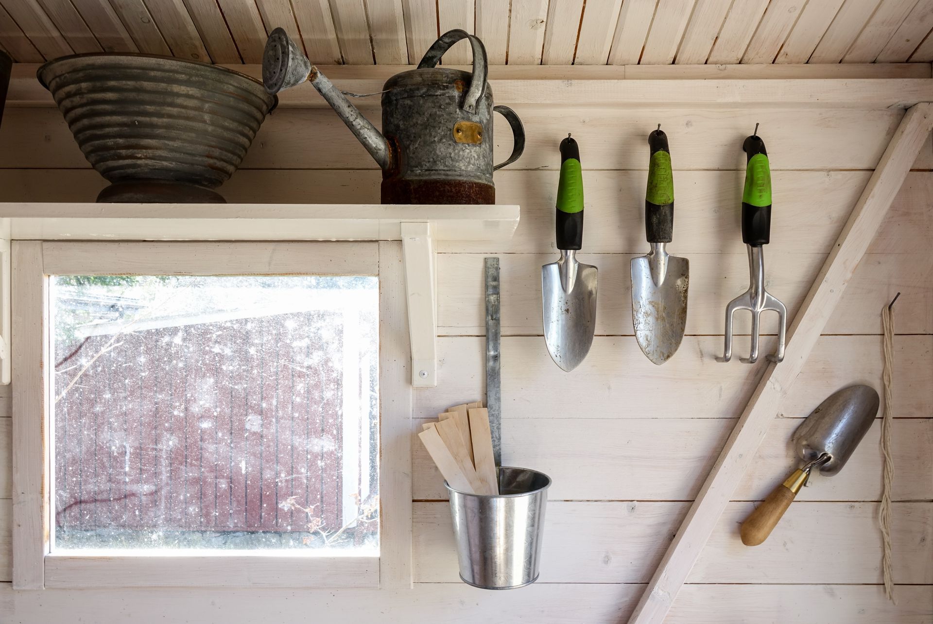 A shelf with a watering can and gardening tools on it