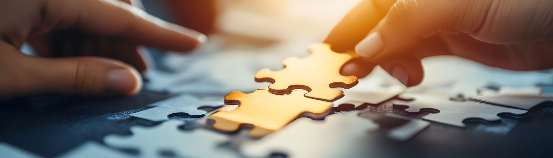 Two hands working together to connect a golden puzzle piece into a larger dark grey jigsaw puzzle.