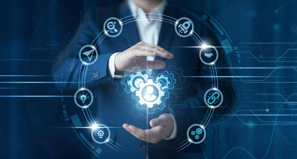 A person in a business suit gestures around a glowing, circular digital interface featuring icons related to technology.