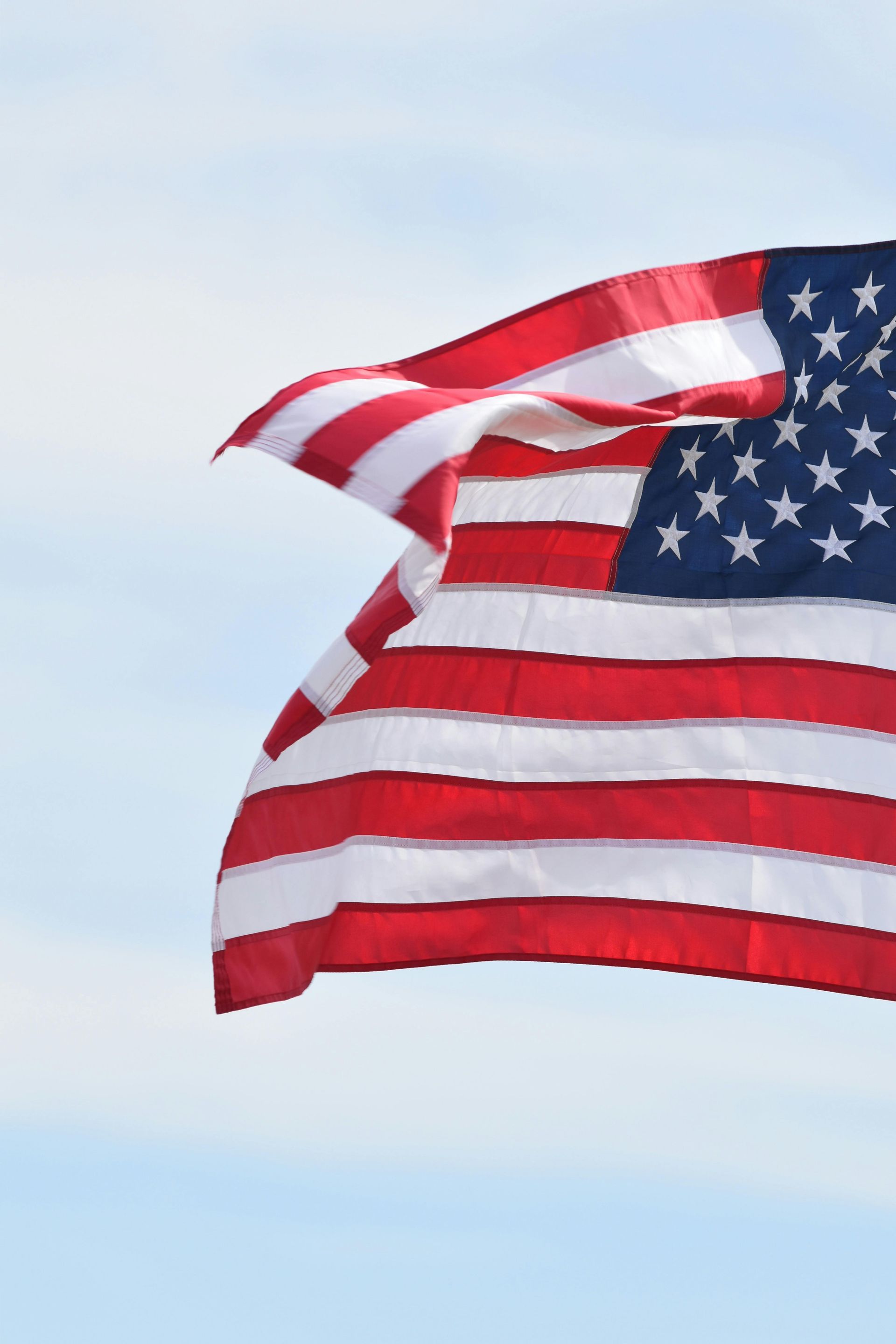 An American flag ripples against a light blue, cloudy sky.