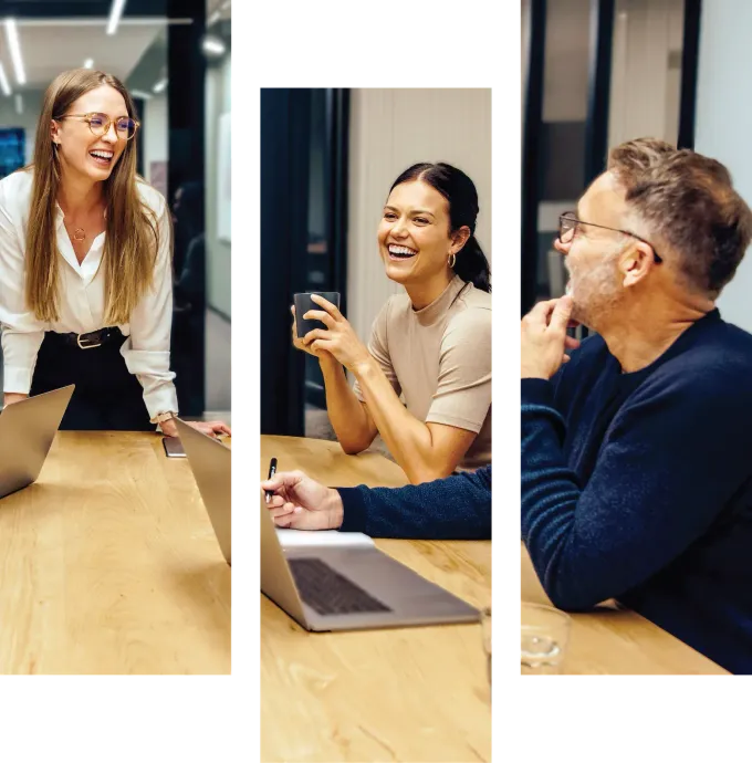 Three coworkers smiling around a conference table in a bright office, discussing a projectIcon