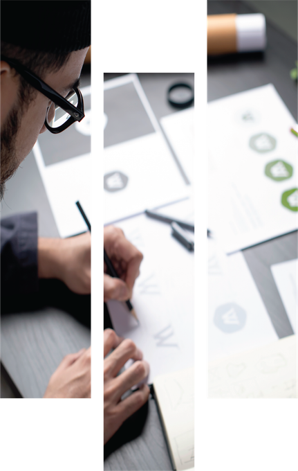 Designer sketching a layout on paper beside printed charts and a pen on a desk
