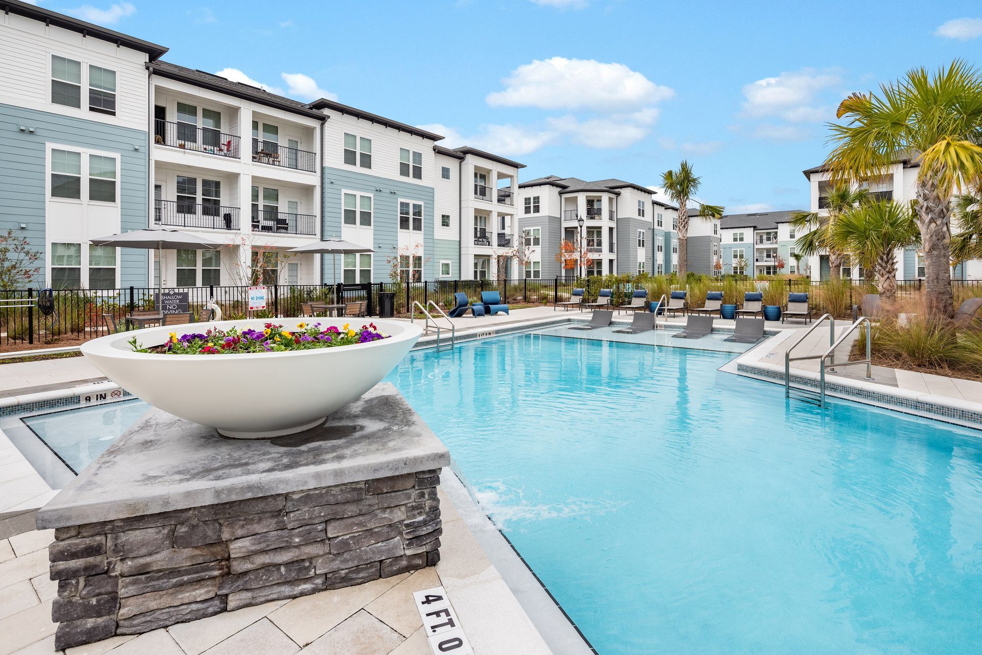 Apartment complex with a pool, blue sky, and palm trees.