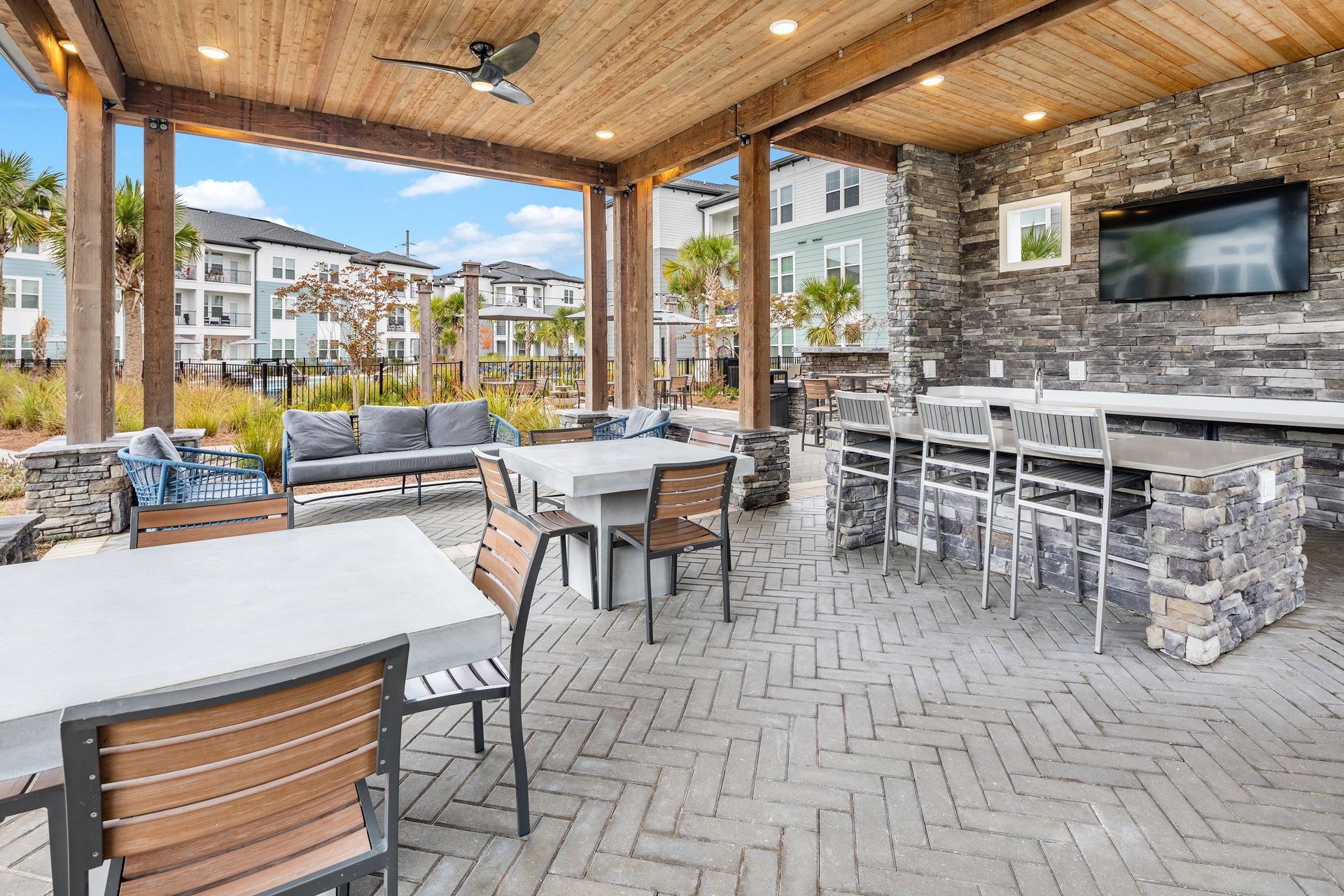 Outdoor patio with tables, seating, TV, and stone features, overlooking a neighborhood.
