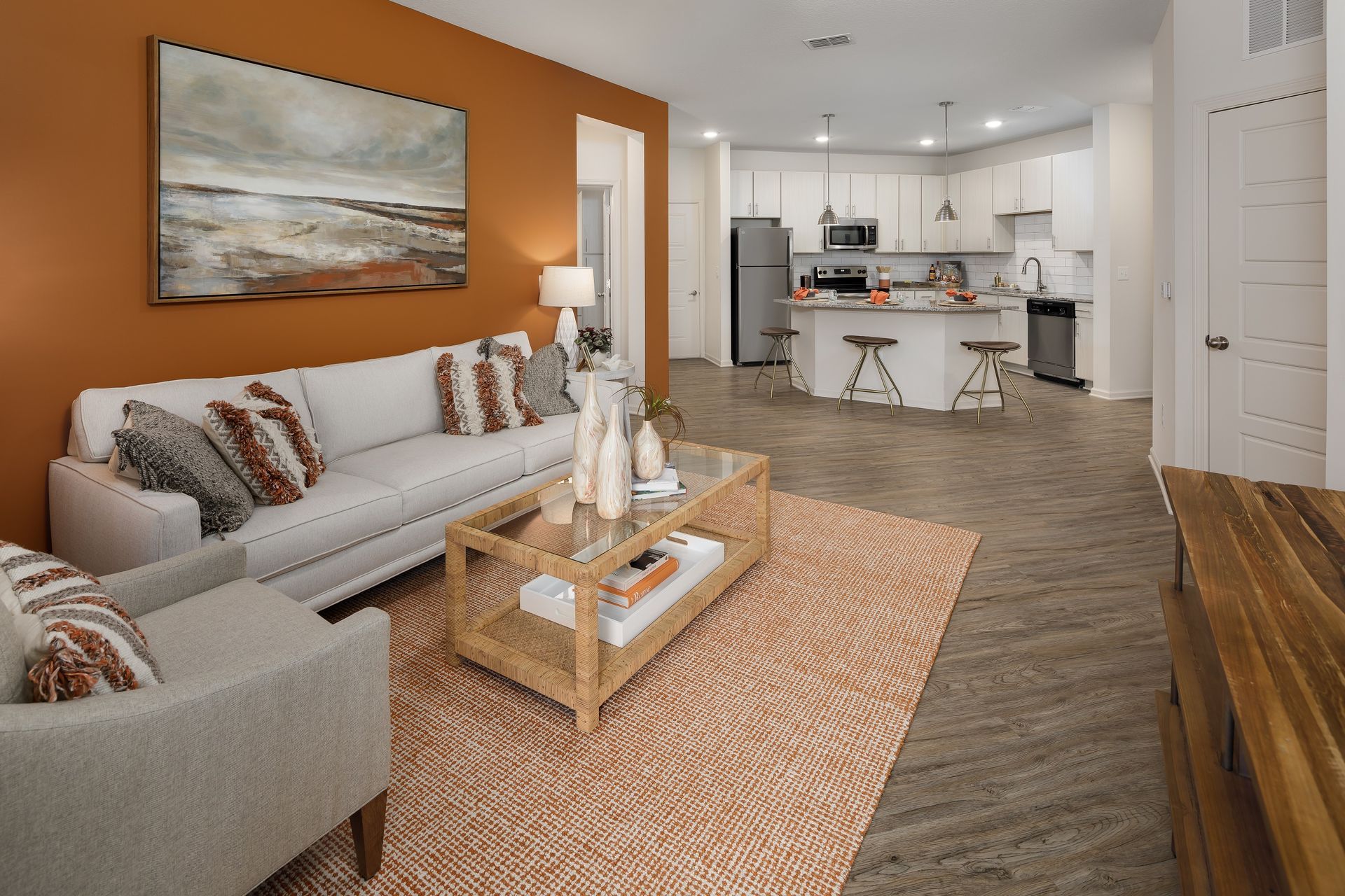 Living room with orange accent wall, white sofa, coffee table, and kitchen in the background.