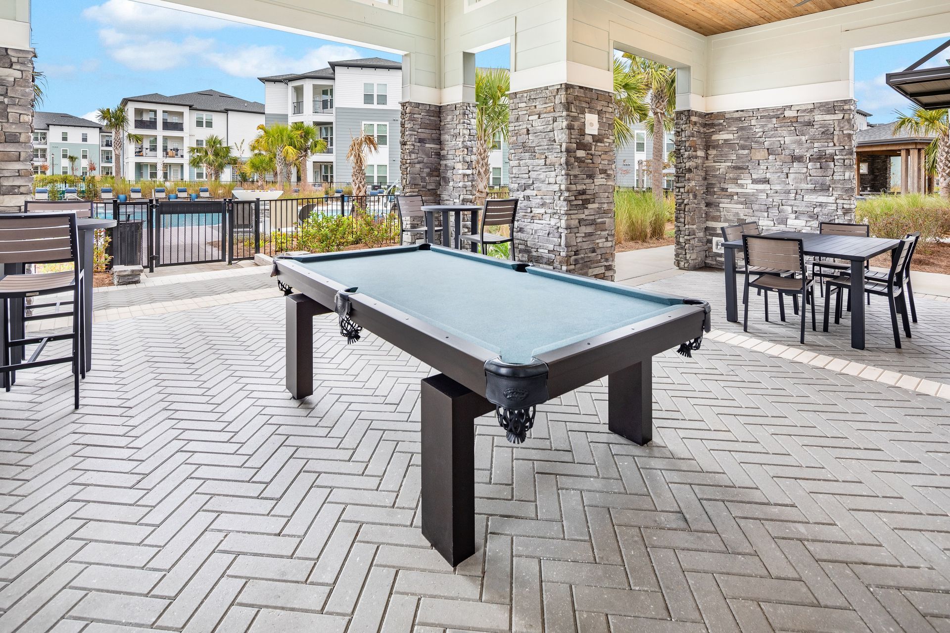 Pool table under an outdoor shaded patio area; other seating and pool in the background.