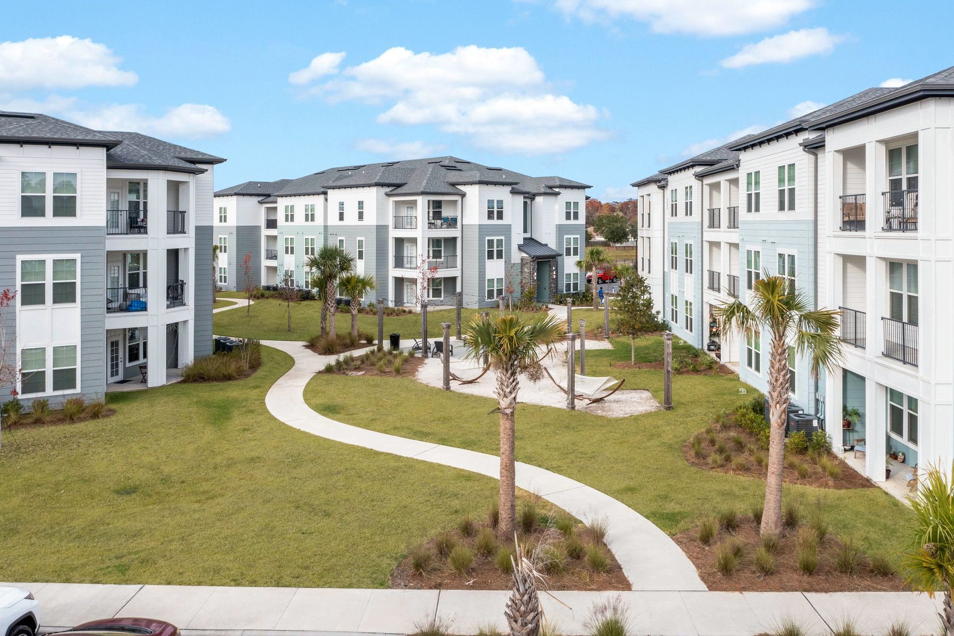 Apartment complex with three-story buildings around a grassy courtyard with palm trees and winding paths.