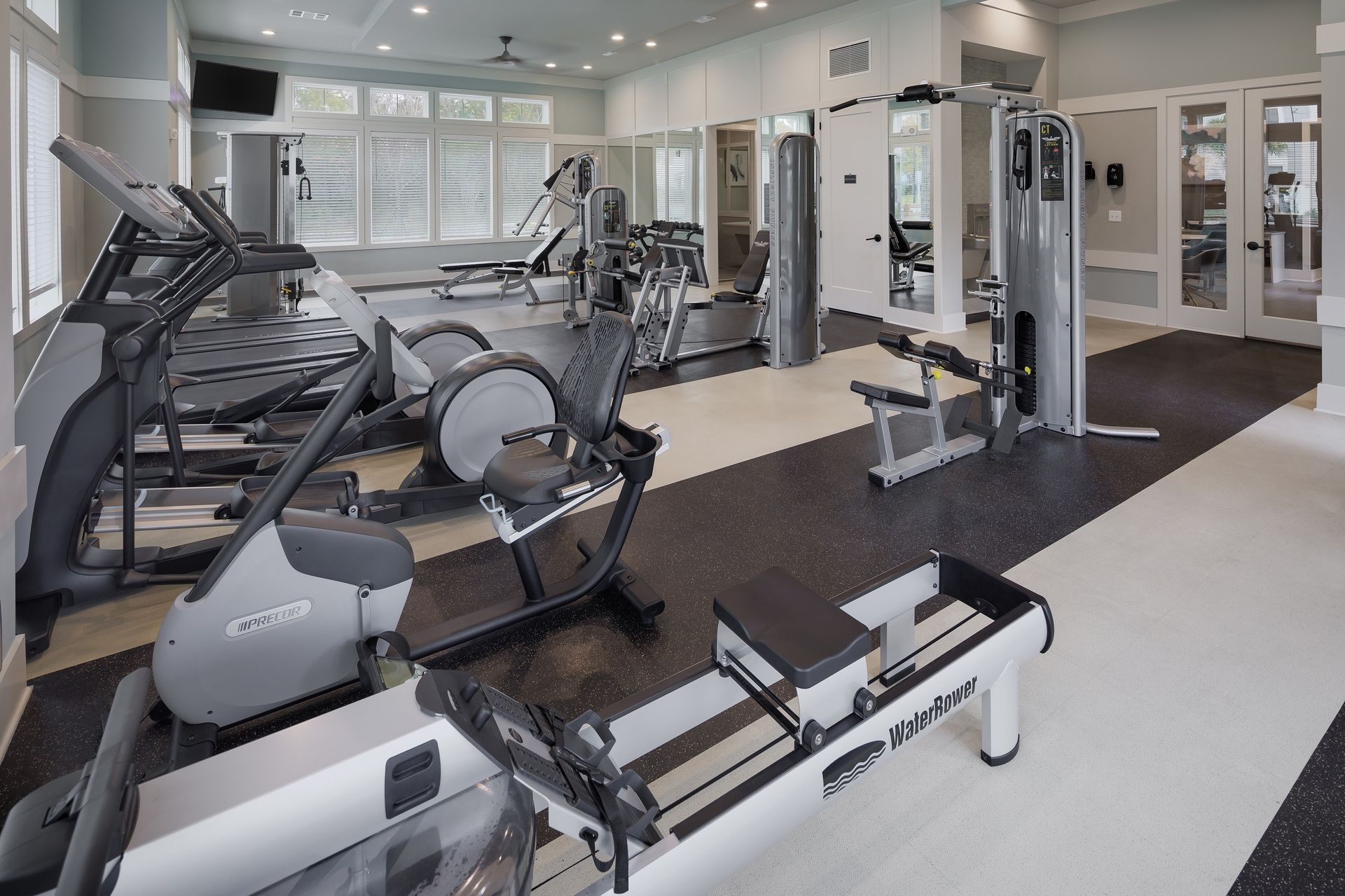 Gym interior with exercise equipment on a black and white floor. Cardio machines and weight machines are visible.
