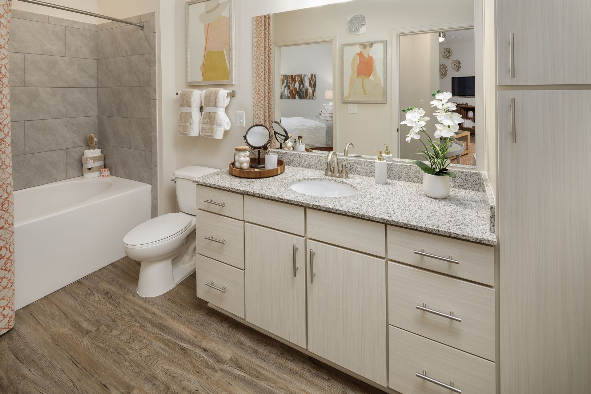 Bathroom with white vanity, tub, toilet, and gray tiled shower, wood-look floors.