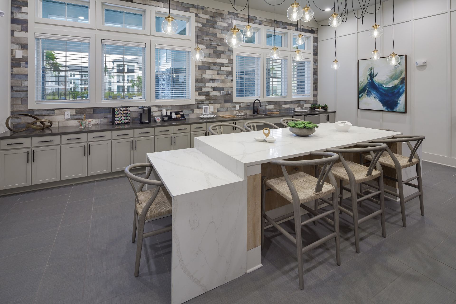 Modern kitchen with island, cabinets, and stone wall. Bar stools surround the island under hanging lights.
