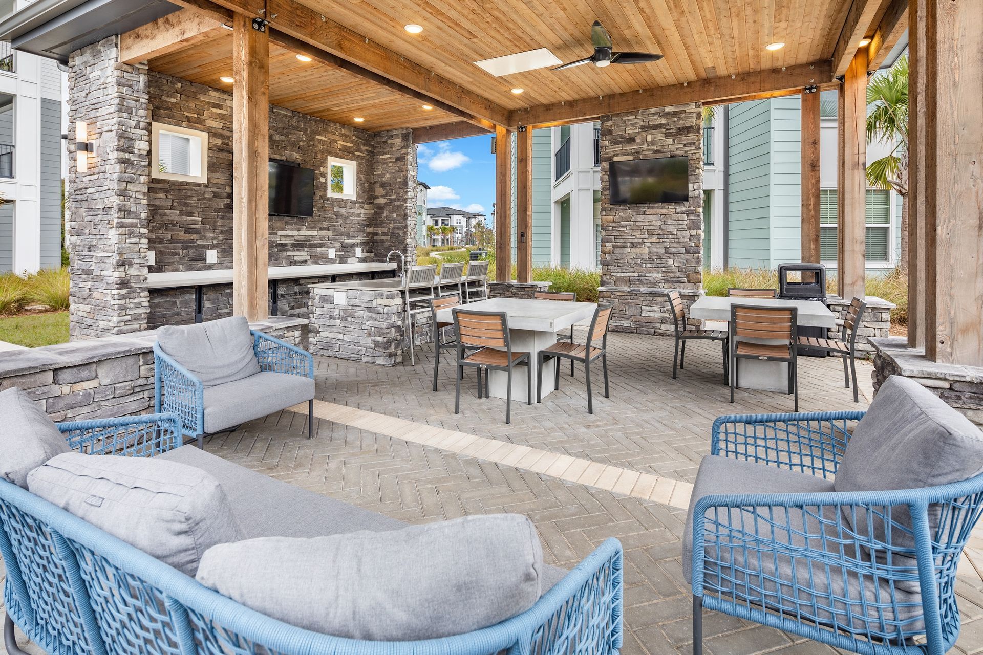 Covered outdoor patio with seating, tables, TVs, and a stone wall.