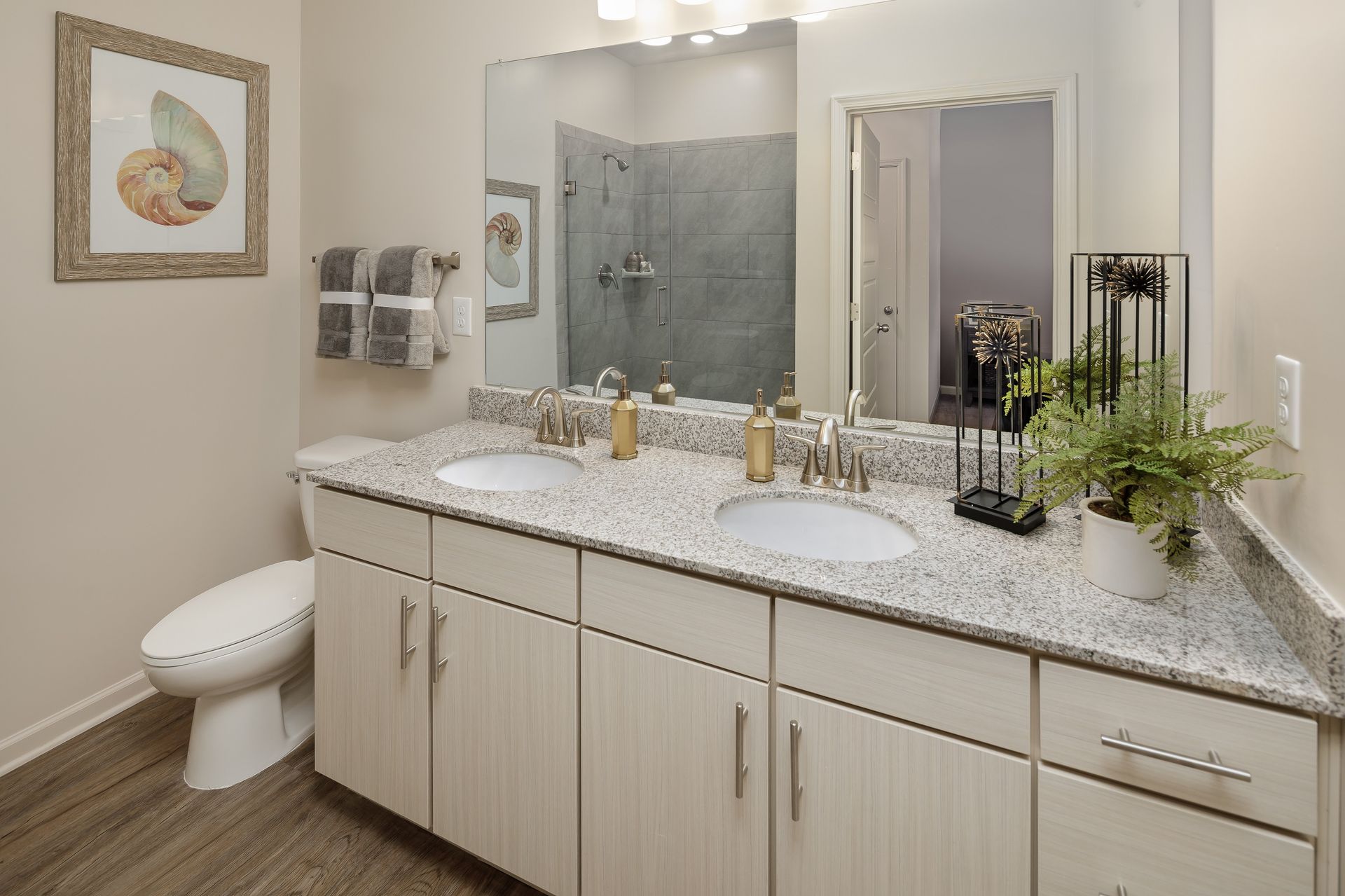 Bathroom with a double vanity, granite countertop, and walk-in shower. Coastal decor with seashells and plants.