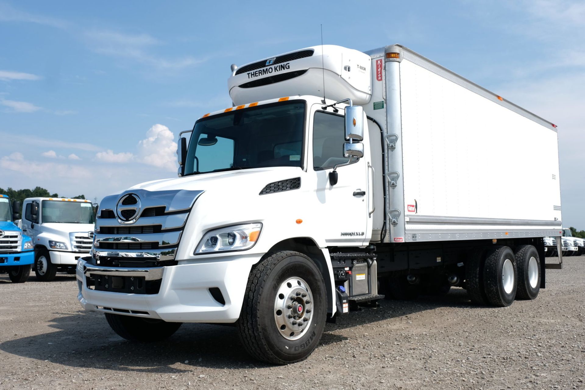 White refrigerated box truck parked on gravel, under a blue sky.