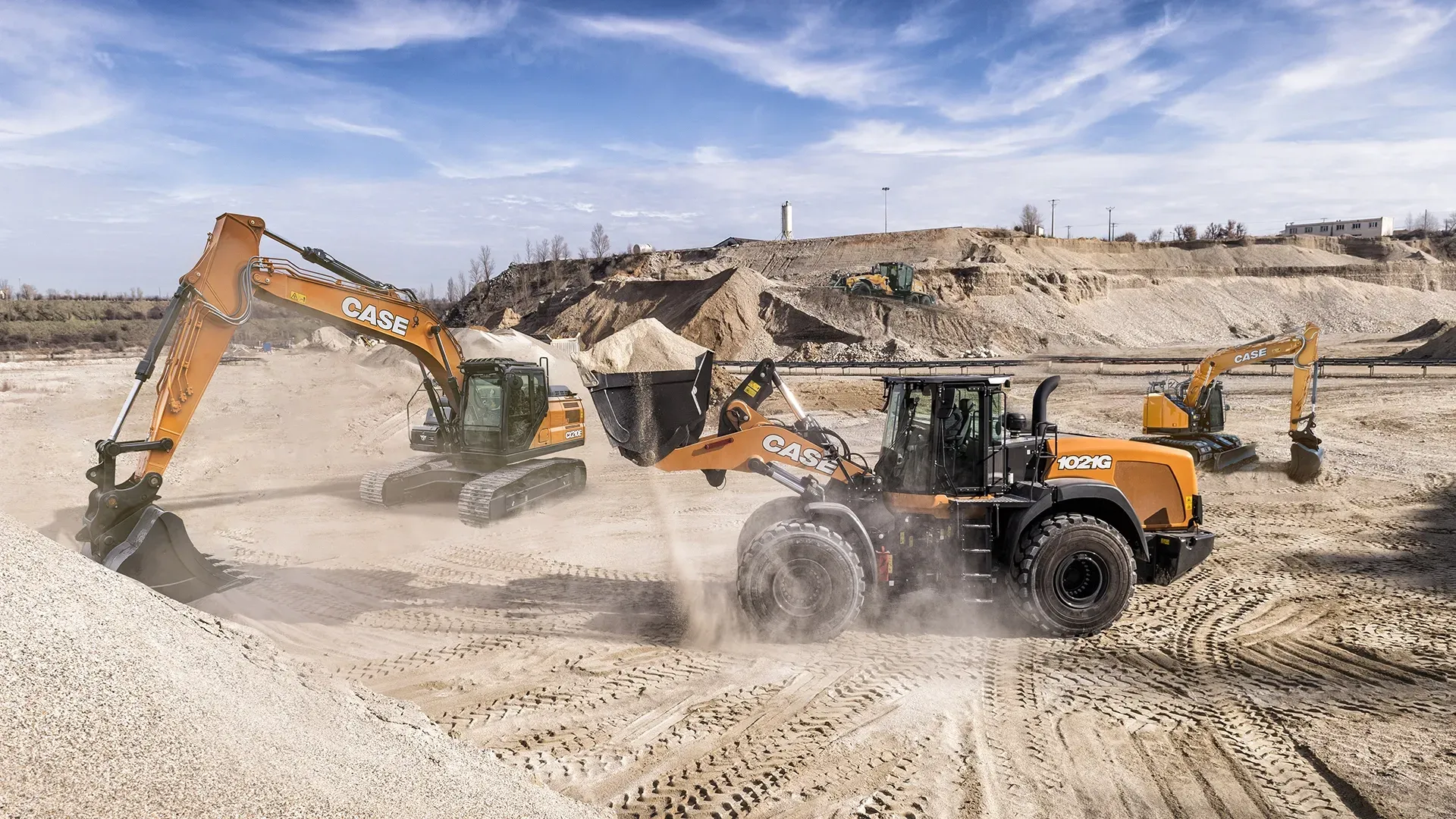 Construction site with excavators and a loader working on a pile of dirt under a blue sky.