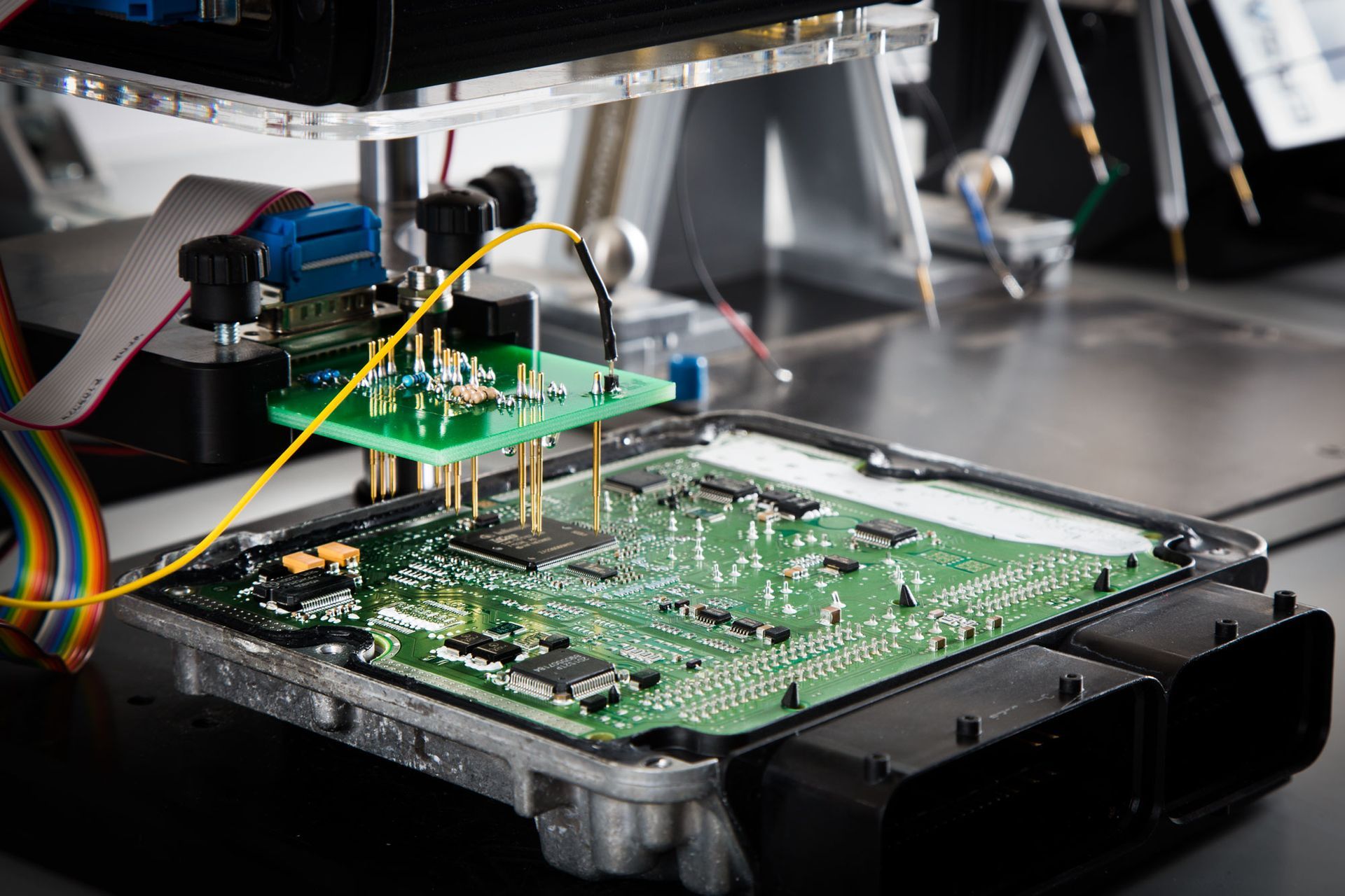 Circuit board being tested with probes, in a laboratory setting. Green and gold components are visible.