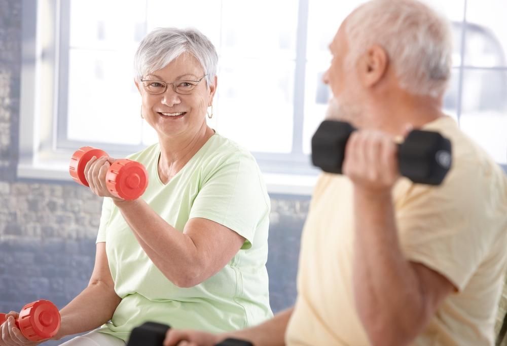 A man and a woman are lifting dumbbells in a gym.
