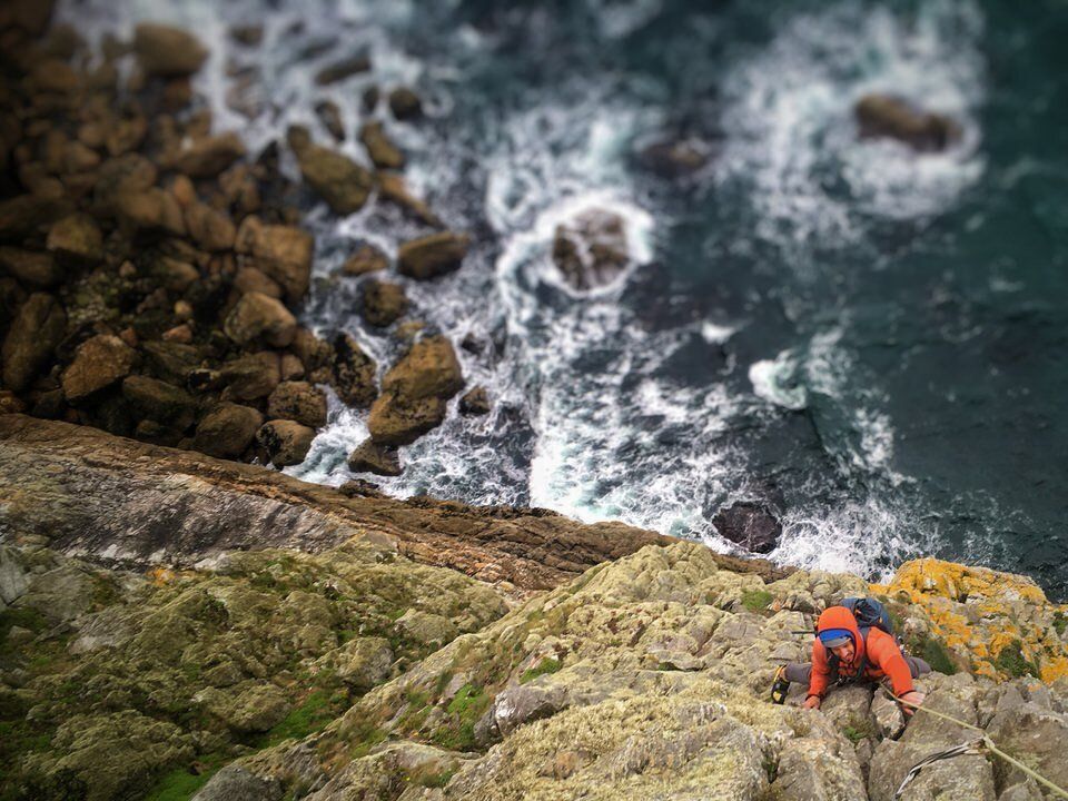 Climber ascending a cliff above the sea