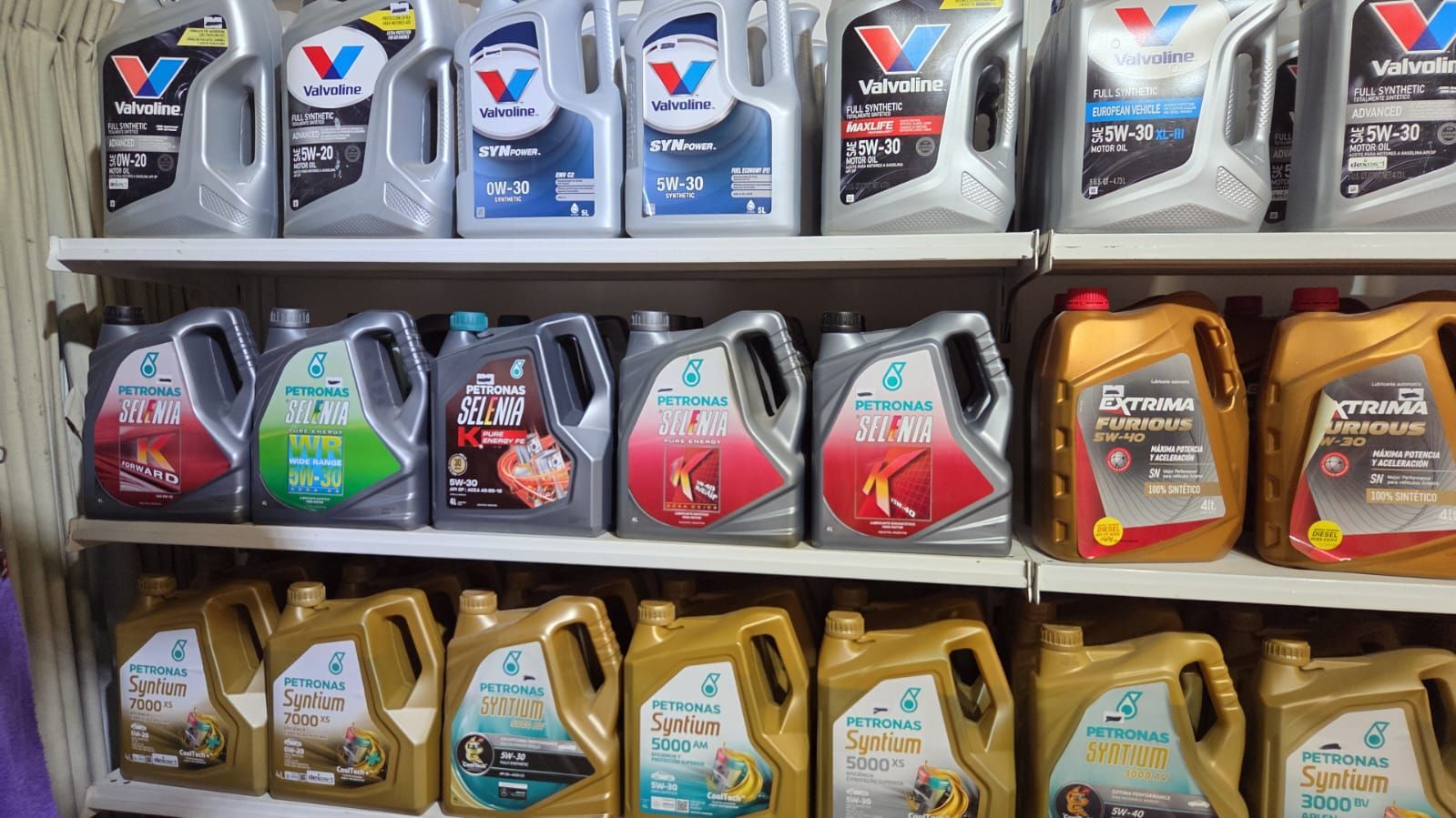 Un expositor en un estante de tienda con varios envases de aceite de motor de diferentes colores y marcas.