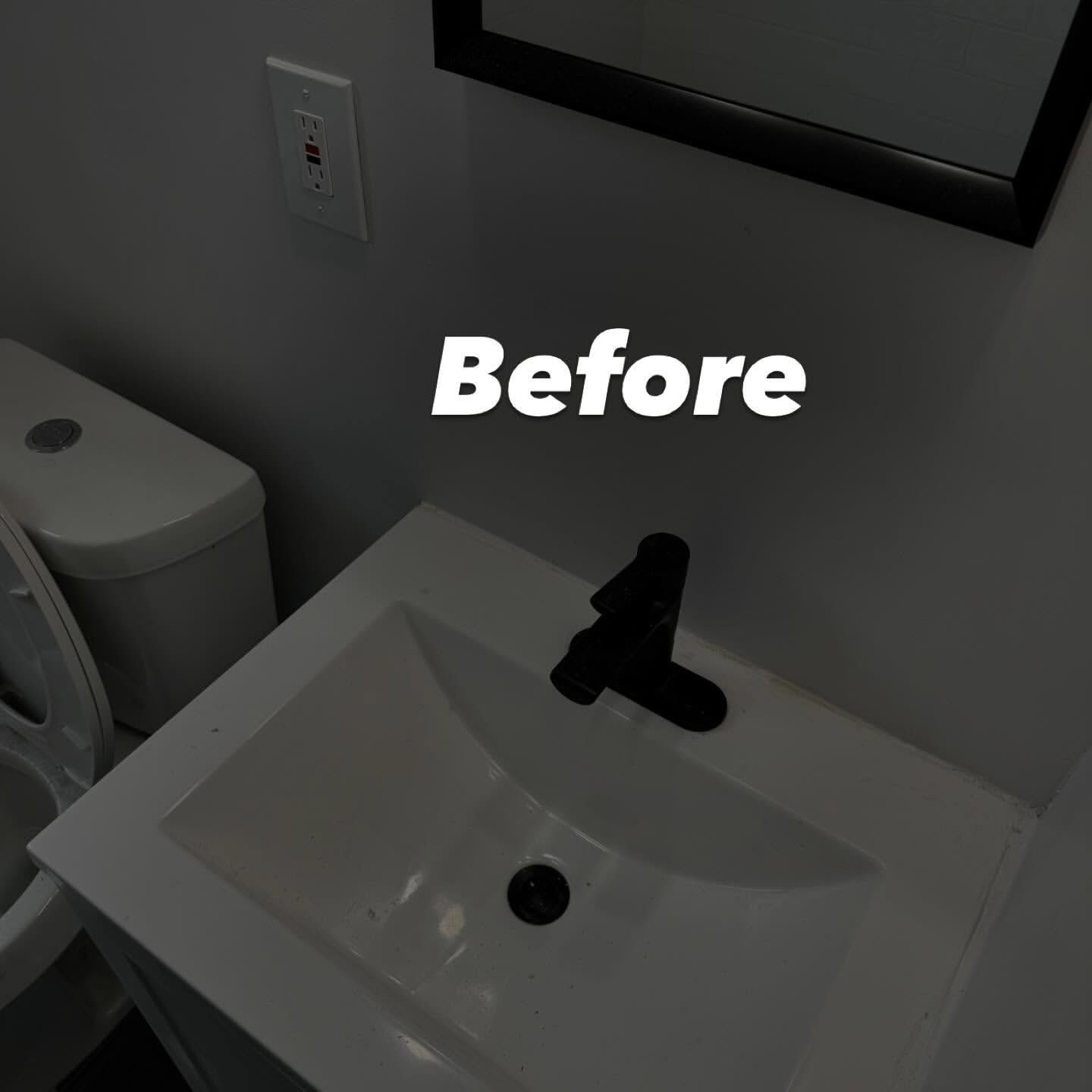 Bathroom sink with black faucet, white countertop, and toilet in gray-walled room.