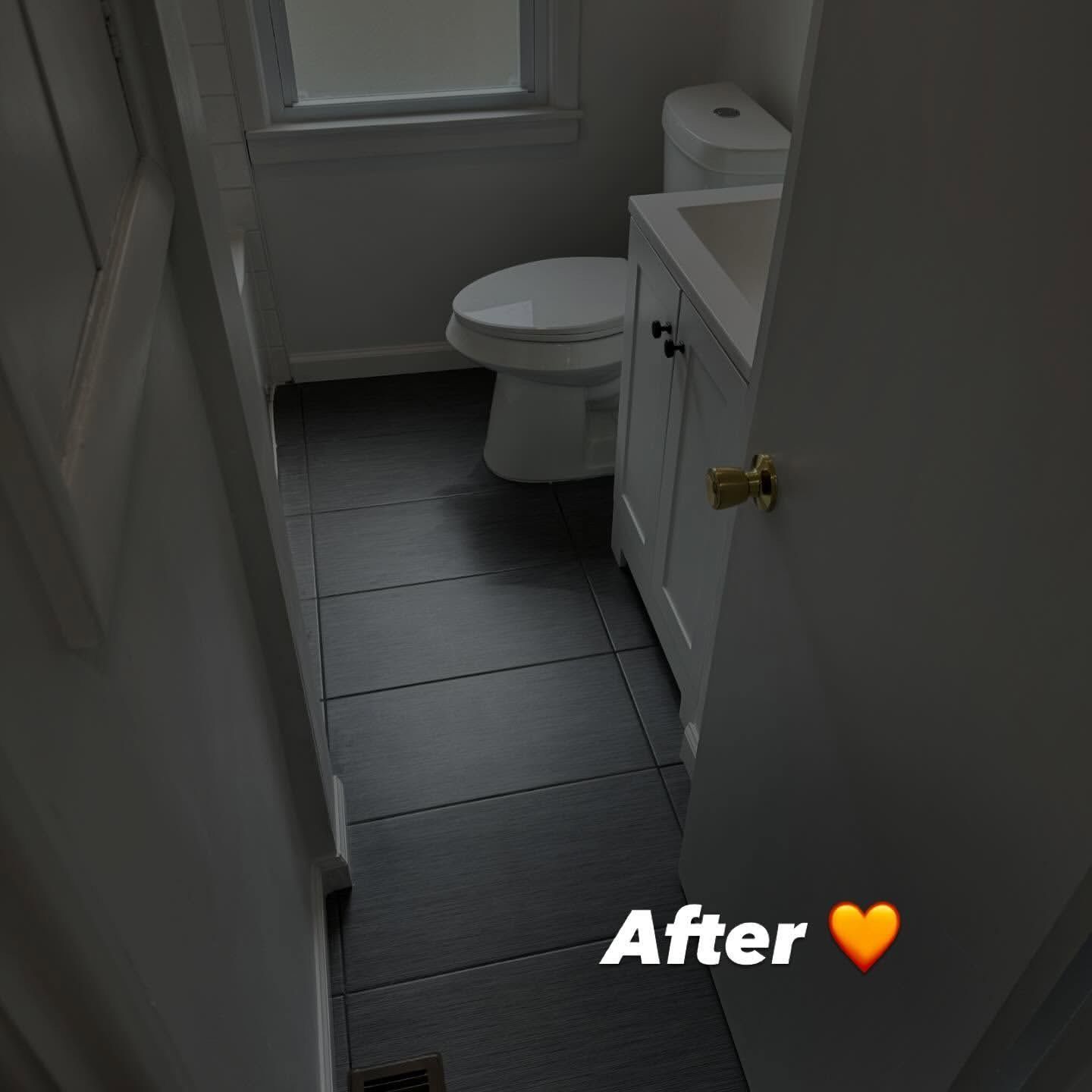 Bathroom with dark gray tile floor, white toilet, vanity, and door. 