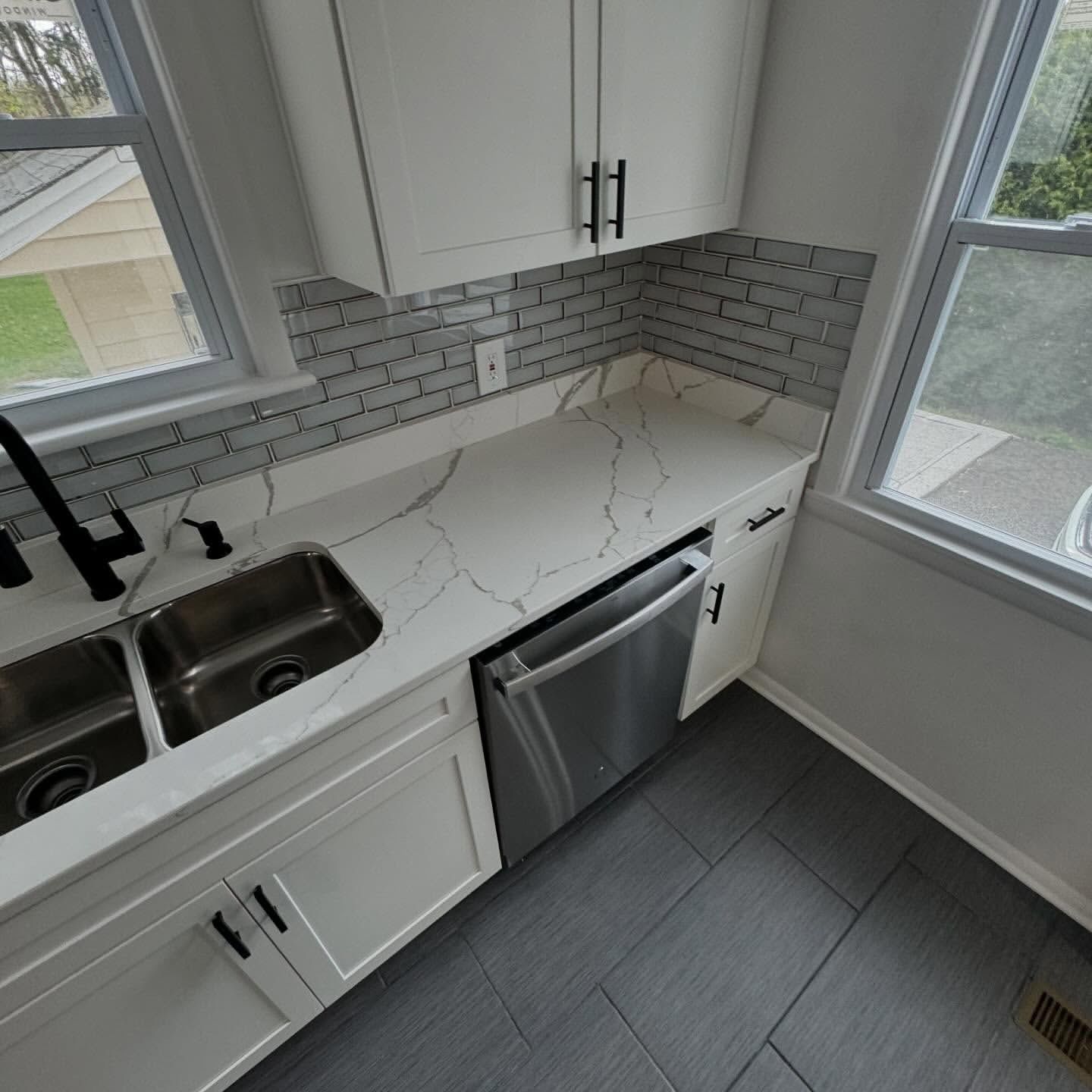 White kitchen with stainless steel appliances, white countertops, and grey backsplash.