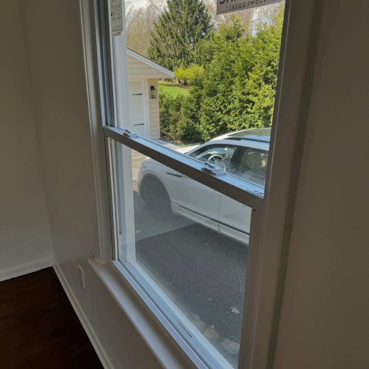 A window in a white frame with a view of a driveway, car, and trees outside.