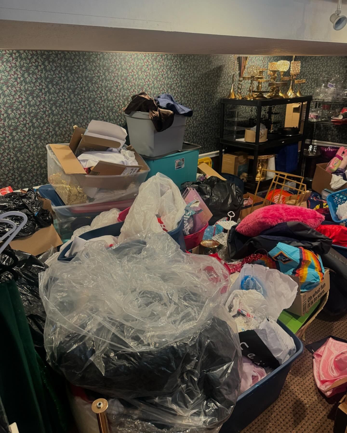 Cluttered room with piles of clothes, boxes, and storage bins.