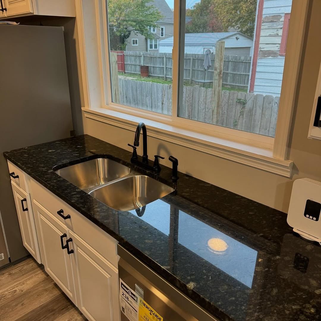 A kitchen with a black granite countertop, white cabinets, and a double sink under a window.