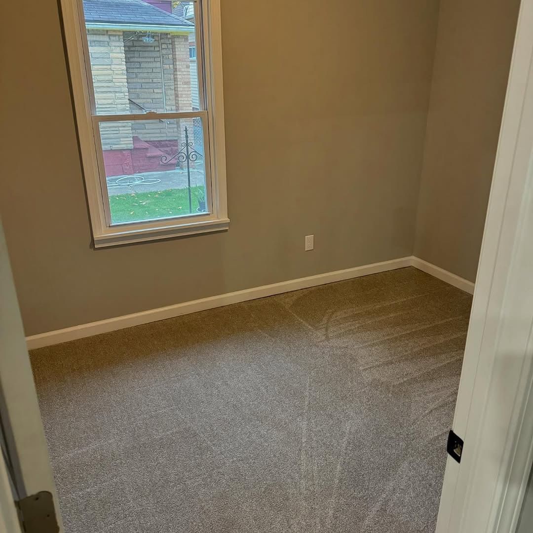 Empty room with tan walls, gray carpet, small window, and door.