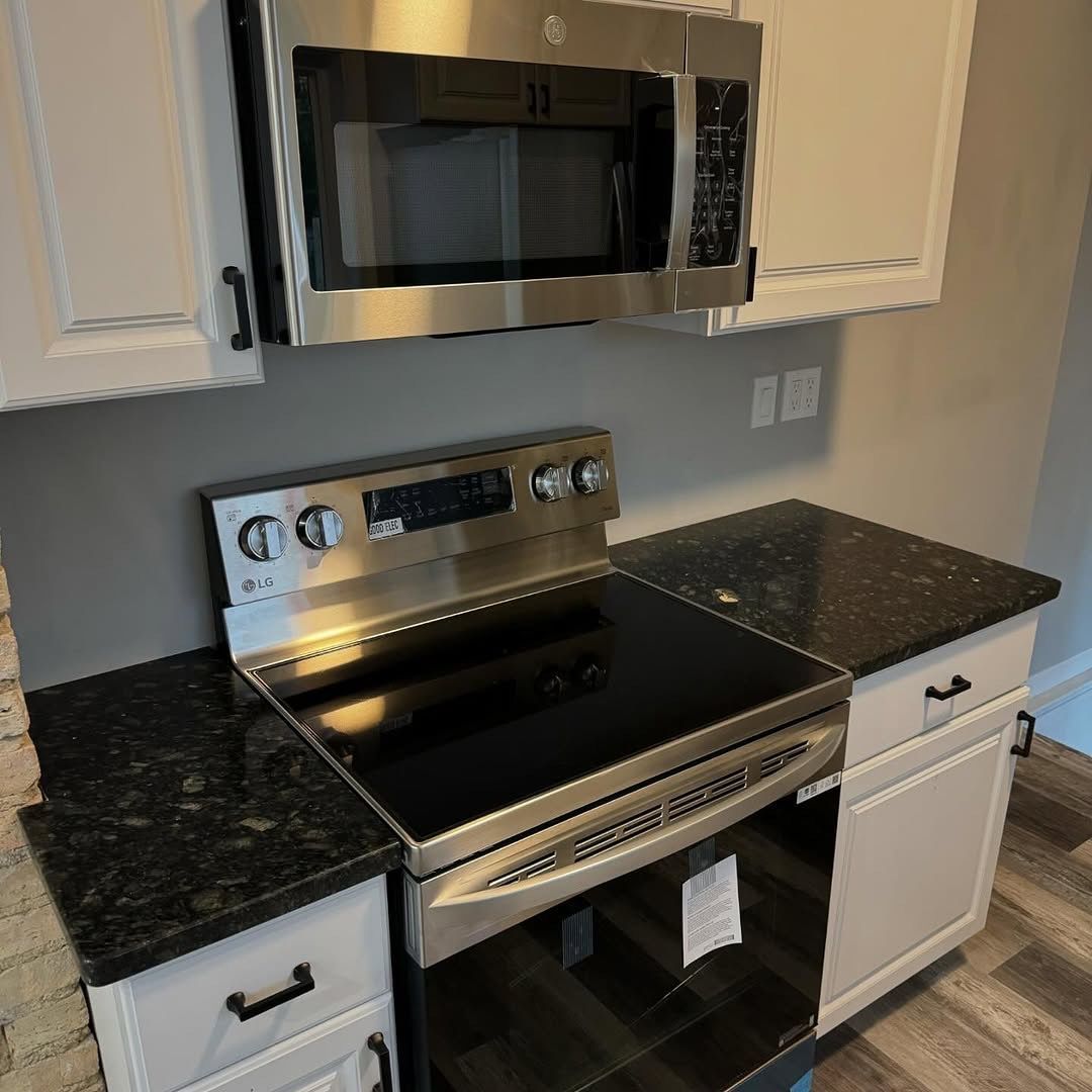 Stainless steel range and microwave in a kitchen with dark countertops and white cabinets.