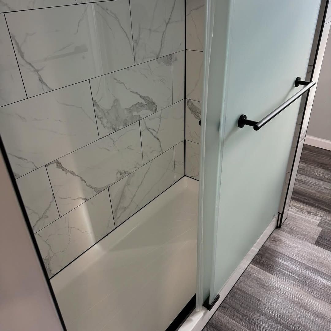 Shower stall with frosted glass door, marble-patterned tile, and black hardware.