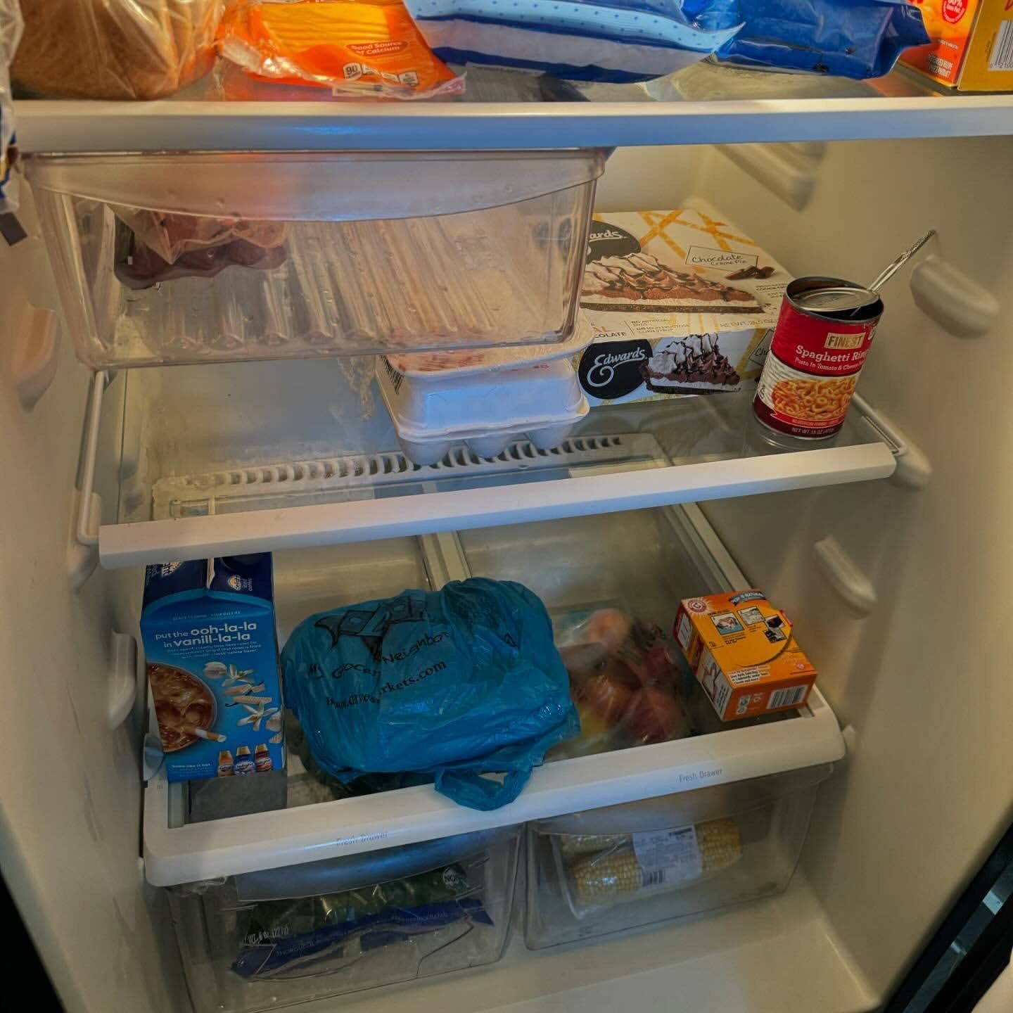 Refrigerator interior, showing shelves with various food items including a bag, cartons, and a can.