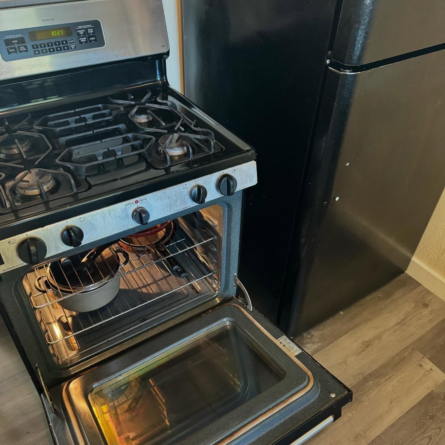Stovetop and oven open, a pot inside. Black refrigerator next to it.