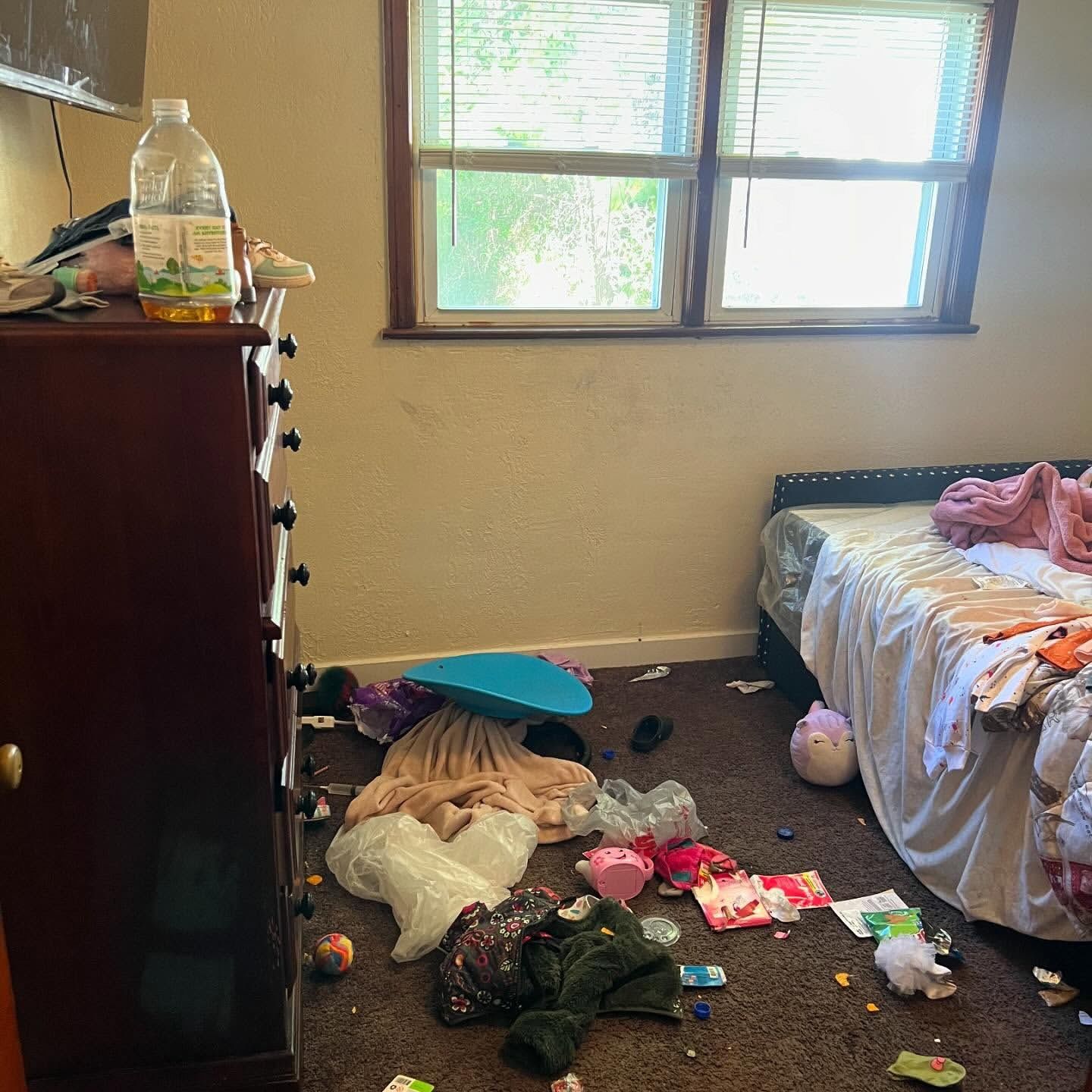 Messy bedroom with clothes, trash, and a cluttered dresser.