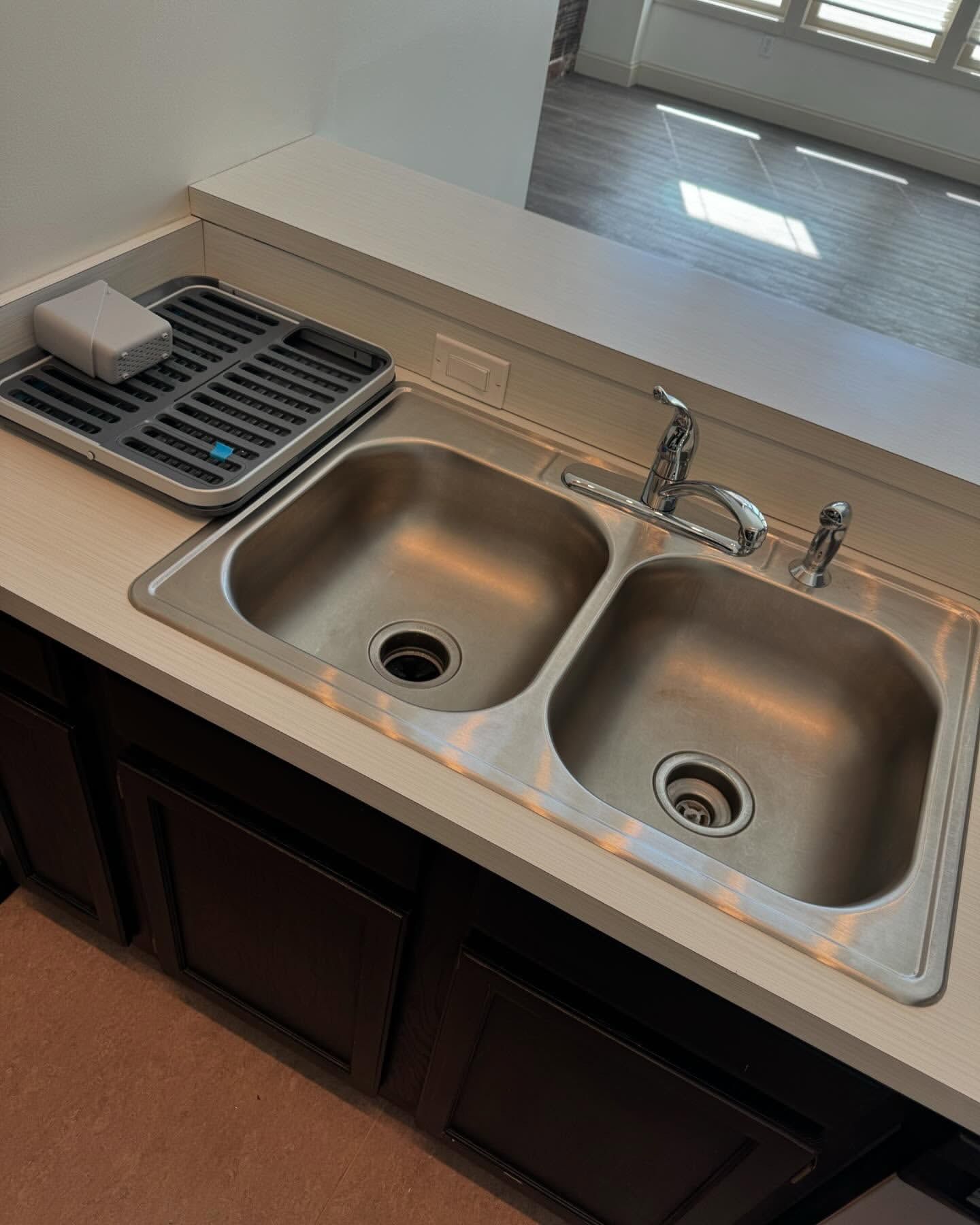 Stainless steel double kitchen sink with a dish drying rack on a white countertop above dark cabinets.