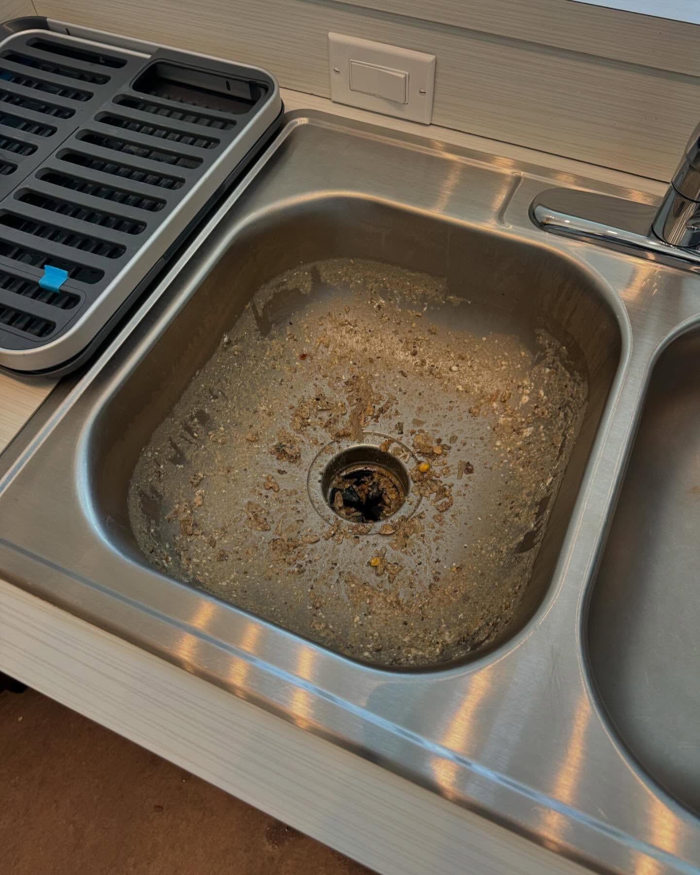Dirty kitchen sink with food debris around the drain.