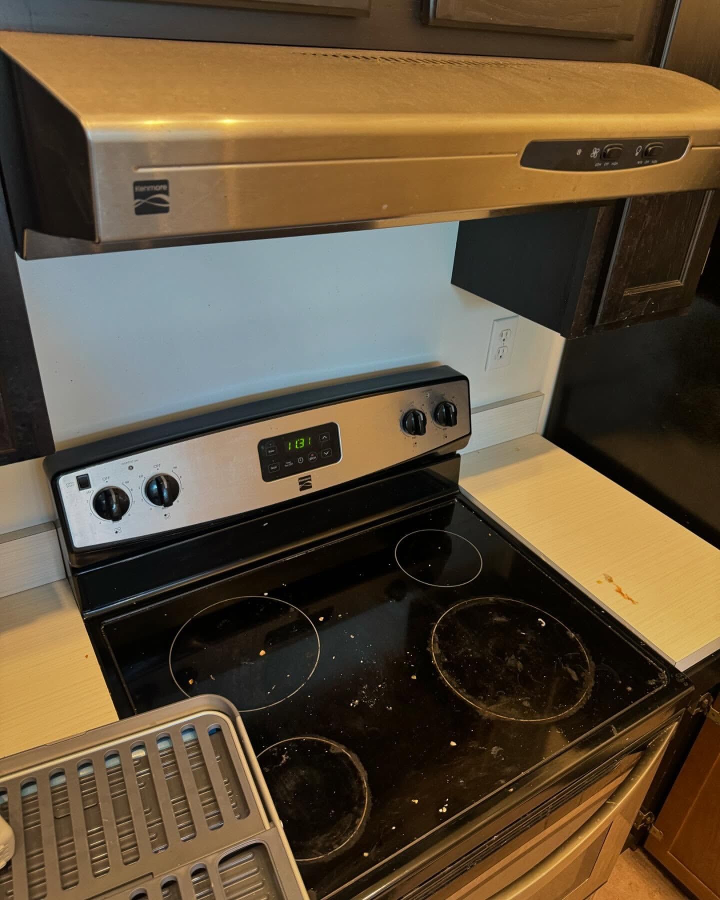 Kitchen stove with a stainless steel hood above it. The stove top is black with four burners.
