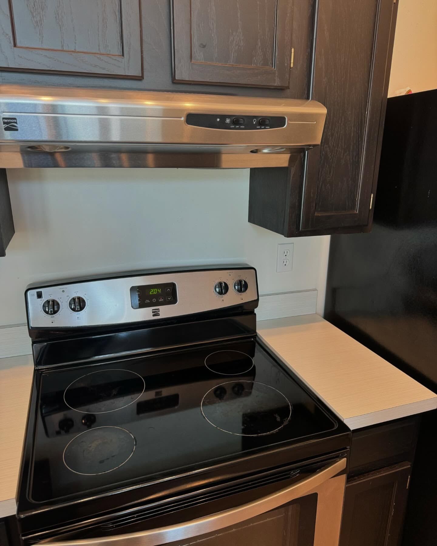 Stove with black cooktop and stainless steel hood in kitchen with dark cabinets.