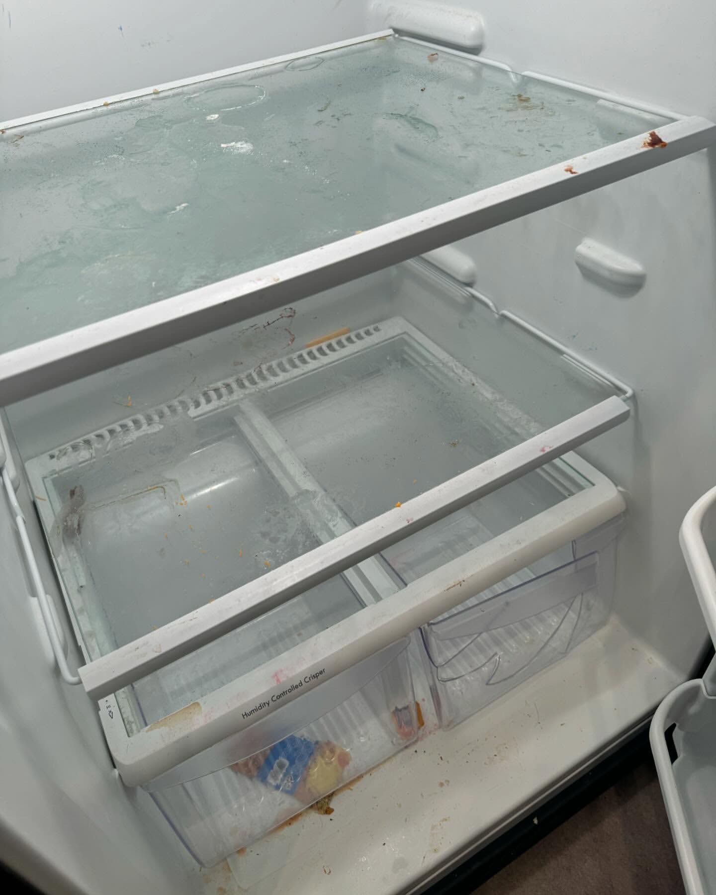 Inside of a dirty refrigerator with glass shelves, showing frozen food and spills.