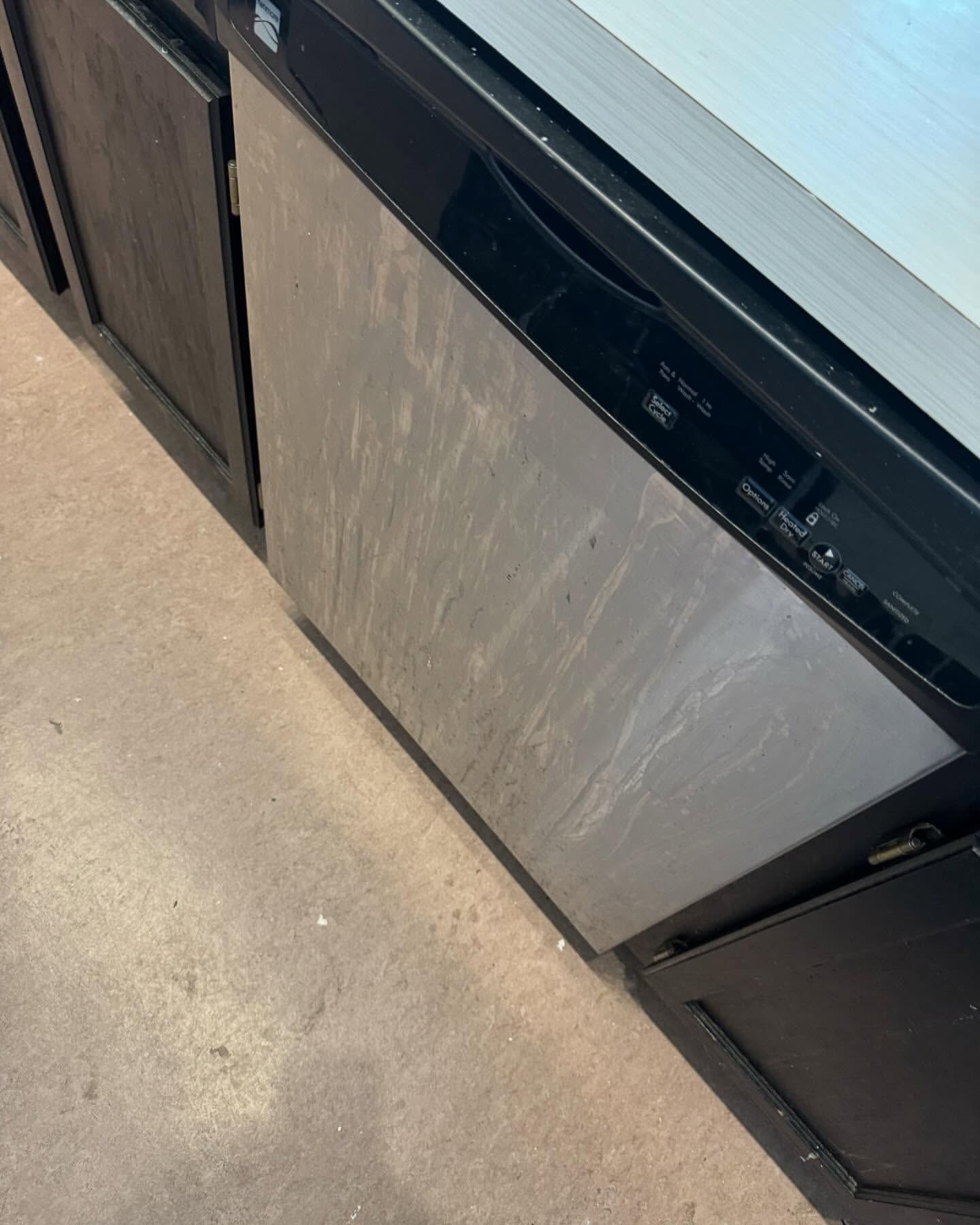 Stainless steel dishwasher in a kitchen, with dark cabinets.